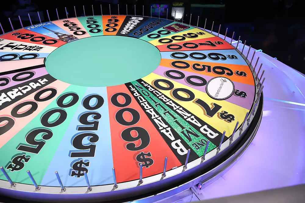 Close-up view of the colorful Wheel of Fortune LIVE! prize wheel on stage, featuring wedges with cash values, prizes, and destinations such as France, separated by silver pegs around the edge.