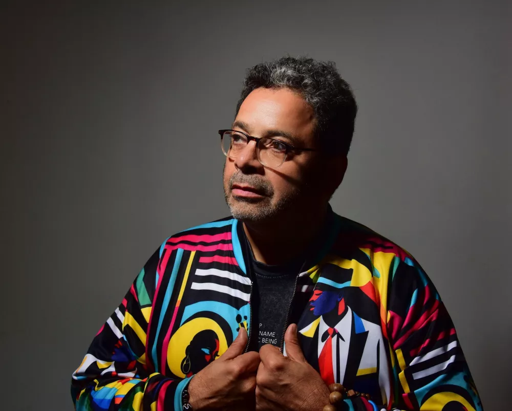 Man wearing a colorful geometric jacket, holding on to the sides of the jacket and looking away.