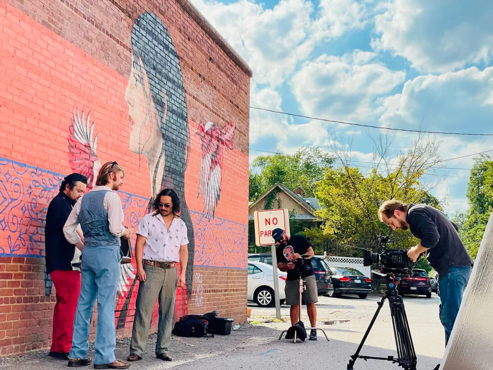 3 people standing in front of a mural being filmed.