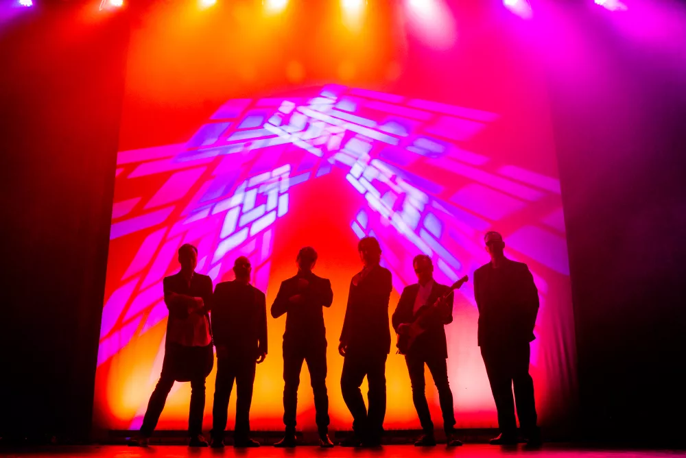 Group of 6 people backlit by red, orange, and magenta lights.