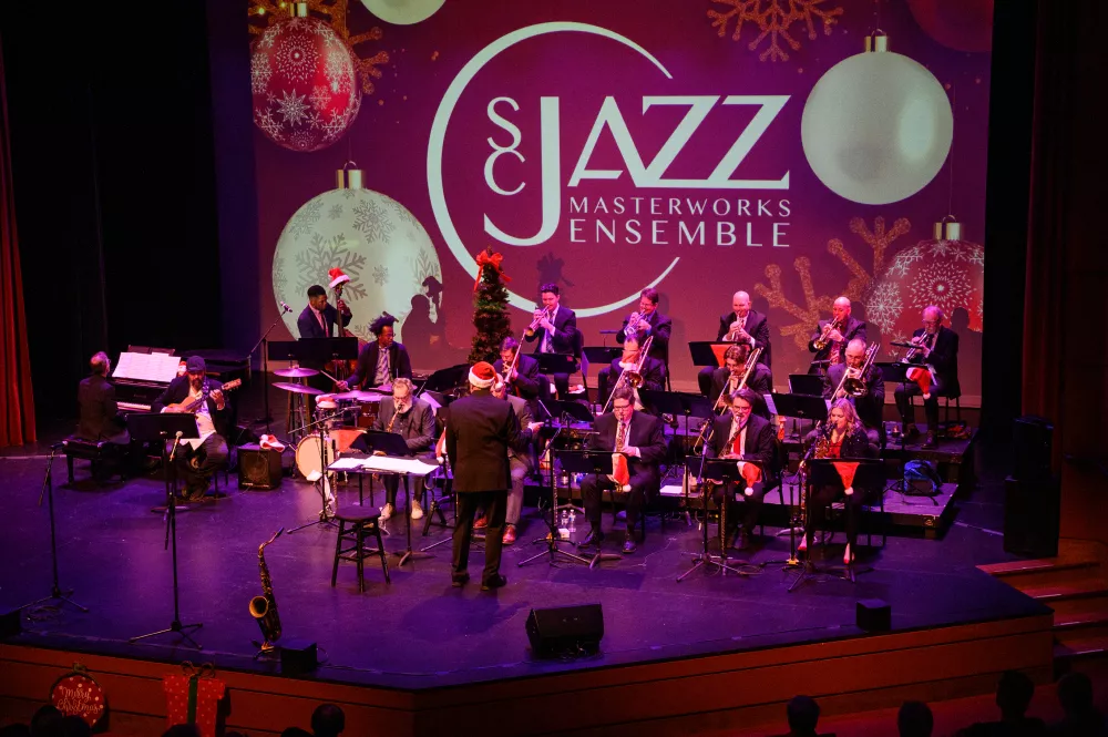 A group of musicians on a stage lit by purple light.