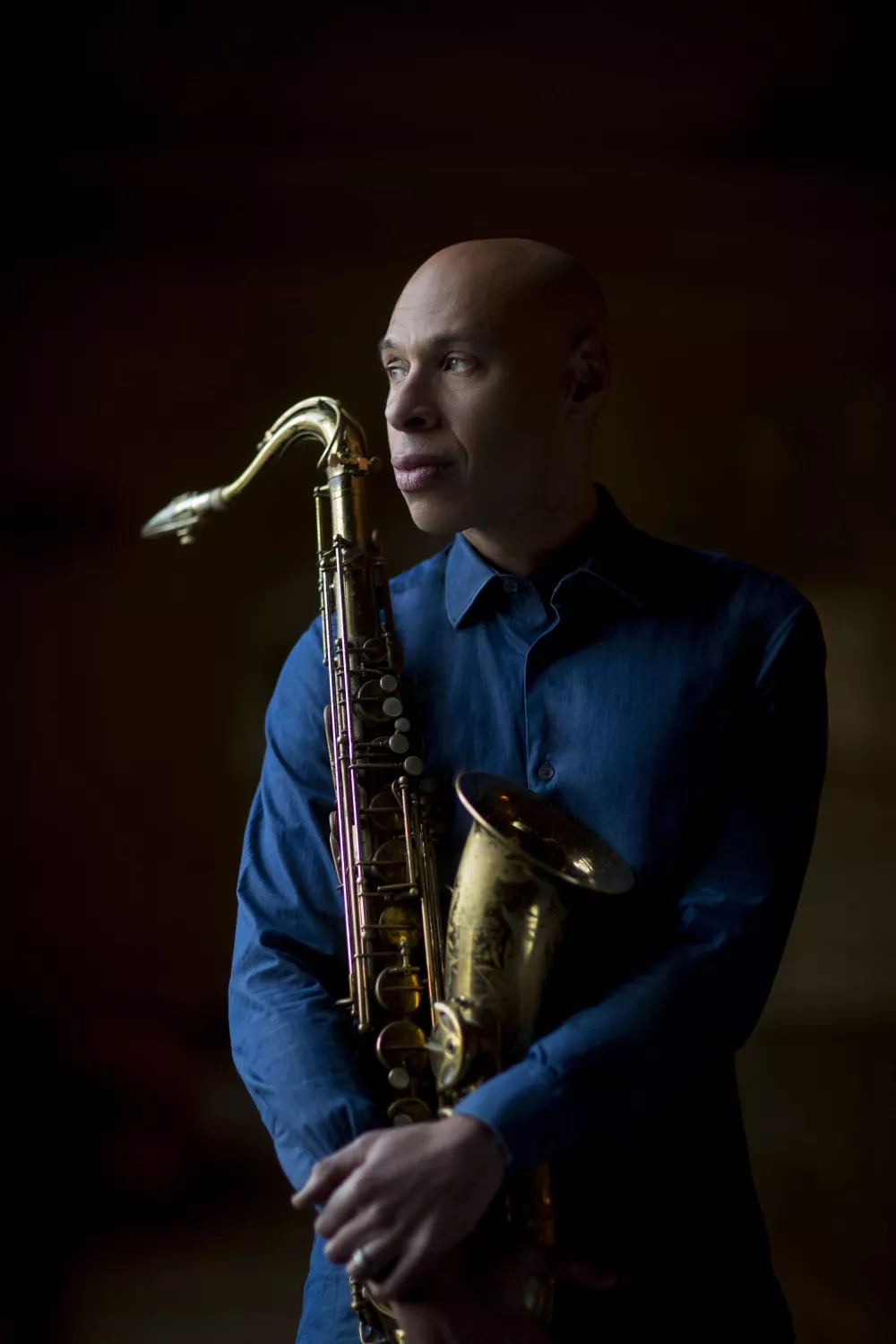 Man in a blue button-down holding a saxophone and looking away.