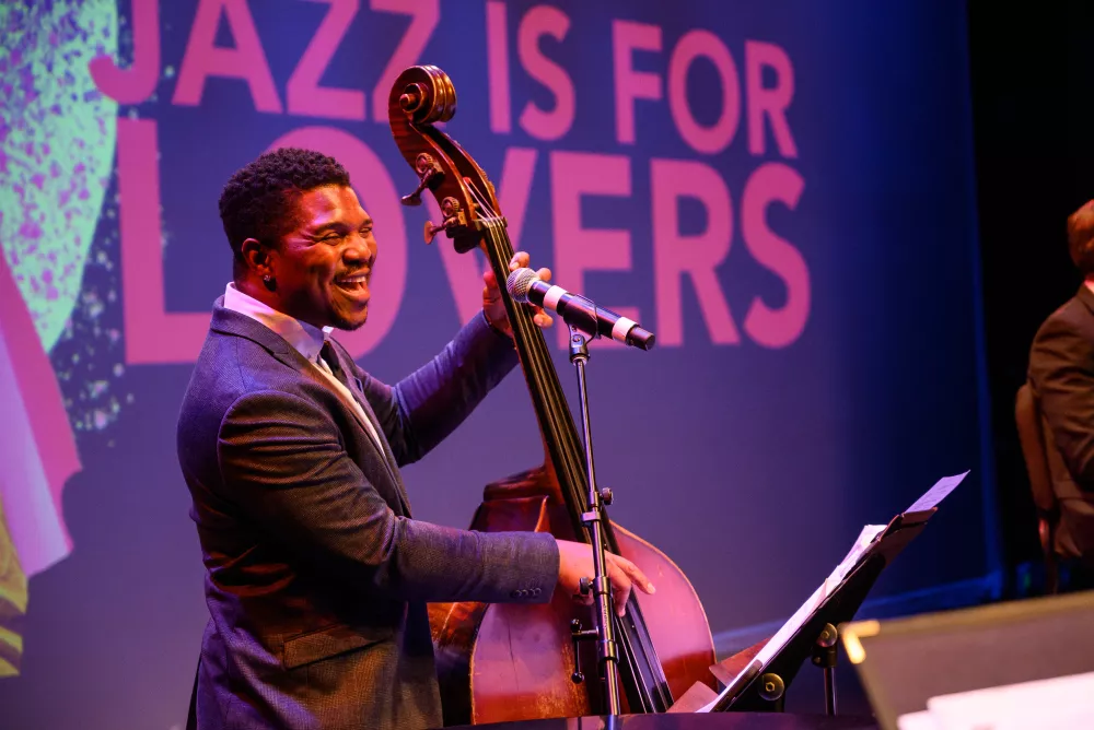 Man in a suit smiling and playing an upright bass.