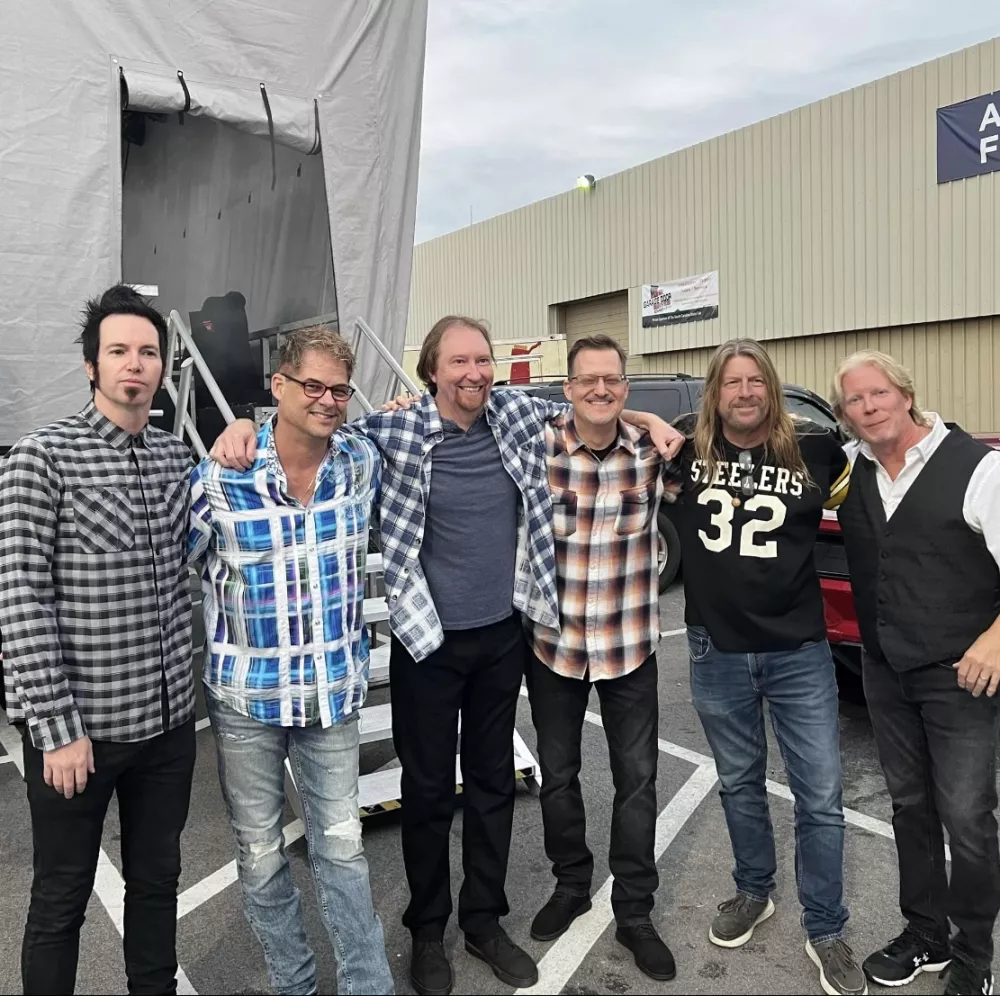 Group of men standing with their arms around each others' shoulders.